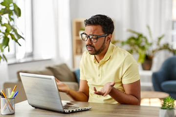 remote job, technology and people concept - sad young indian man in glasses with laptop computer working at home office