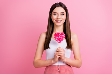 Obraz na płótnie Canvas Photo of charming funny lady hold big heart shape lollipop on stick want to try yummy dessert good mood wear white singlet dotted skirt isolated pastel pink color background