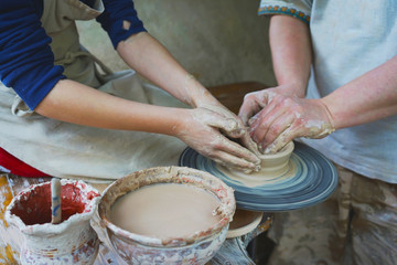 
a master potter teaches a student to work on a pottery wheel.