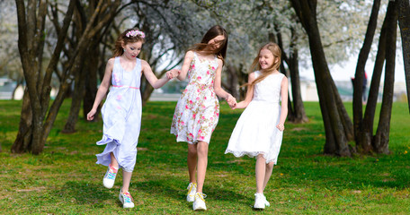 Naklejka na ściany i meble Three beautiful girls in retro dresses for a walk in a flowered garden. The idea and concept of a friendly family and a happy childhood.