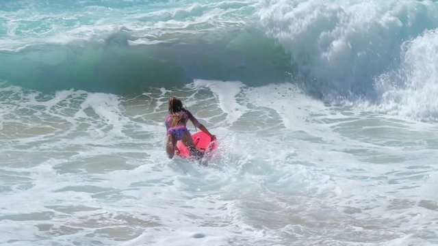 Little girl surfs on the beach break and uses bodyboard as skimboard. Young girl surfer have fun in the waves