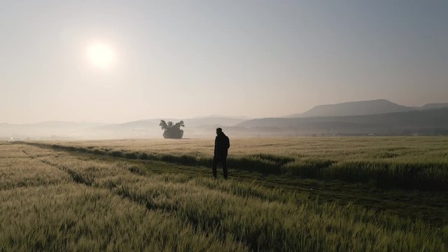 Man walking slowly along a field path towards the sunrise with fog