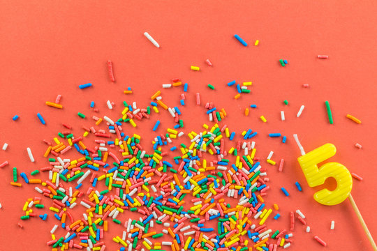 Five Year Old Cake Candle And Birthday Cake Sprinkles On Bright Orange Background