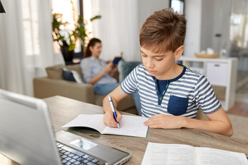 children, education and learning concept - student boy with book writing to notebook at home