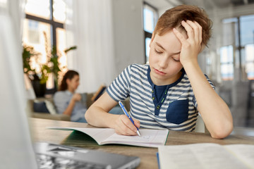 children, education and learning concept - student boy with book writing to notebook at home