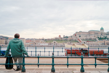 Enjoying vacation in Budapest. Young traveling man sitting on riverside promenade with city view.