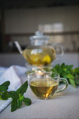 
cup with herbal tea on the background of a teapot with sprigs of mint and flowering branches. Tea Party Concept