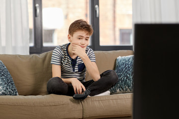 leisure, technology and children concept - sad boy with gamepad playing video game at home