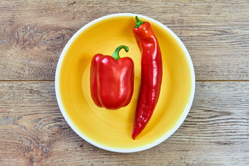 thin and thick pods of different varieties of sweet pepper on a yellow plate on a wooden tabletop