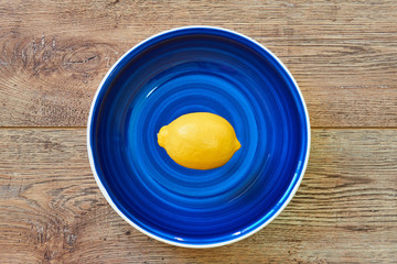 bright yellow lemon on a blue plate on a wooden tabletop