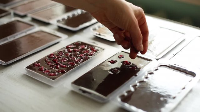 The hand of the chef puts dried fruits into the melted chocolate.