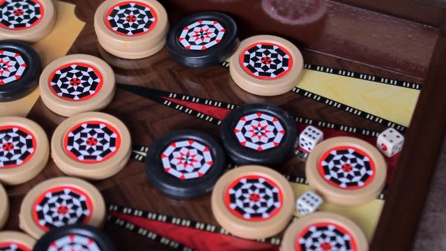Black and white patterned game chips and dice fall on the playing Board from under the backgammon game