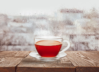 Glass cup of hot tea near window on rainy day