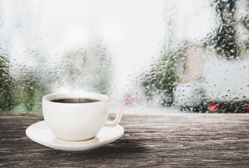 Cup with hot coffee near window on rainy day, space for text