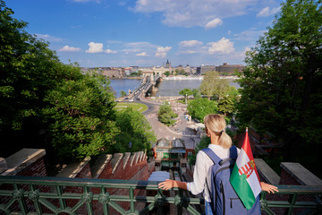 Enjoying vacation in Budapest. Young traveling woman with national hungarian flag walking on riverside promenade with city view.