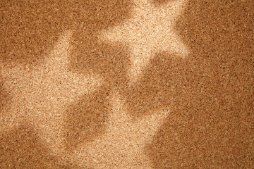 Shadow and light in the form of five-pointed stars on Cork Board.
