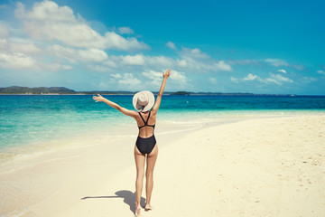 Vacation and freedom. Happy young woman rising hands up standing on tropical beach enjoying beautiful view.