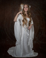 Art photograph of a languid girl in an elven white dress with a barn owl on her shoulder