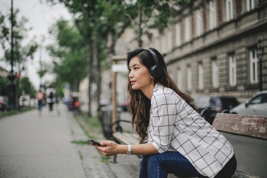 Young woman is listening to music sitting on the bench