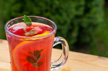 glass goblet with cold cocktail on a wooden table in the garden on a background of green plants