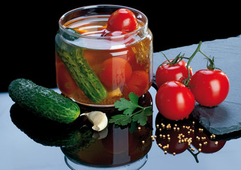 Arranged composition of fresh and canned tomatoes and gherkins on a black background with a mirror reflection.