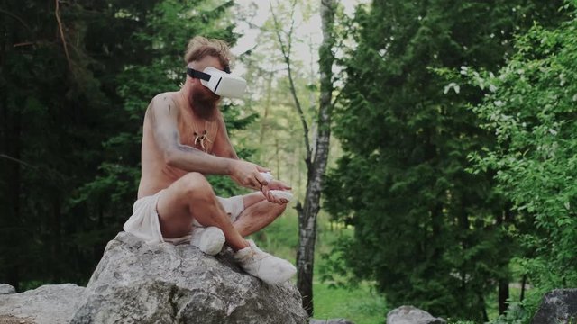 Prehistoric Primeval Human Involved in Cyber Reality with Modern VR Glasses. Using Futuristic High Tech Device with Controller or joystick. Immersive and Entertainment Concept.
