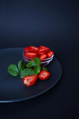 
glass bowl with fresh strawberries and green leaves on a black background