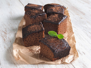 Freshly baked classic brownie on parchment are laid out on a white wooden surface.