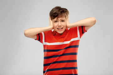 people, noise and stress concept - boy closing ears with hands over grey background