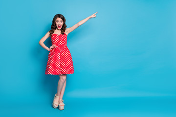 Full length photo of attractive lady hold arm direct finger far away traveler showing way excited mood wear red white dotted retro dress summer open toe shoes isolated blue color background