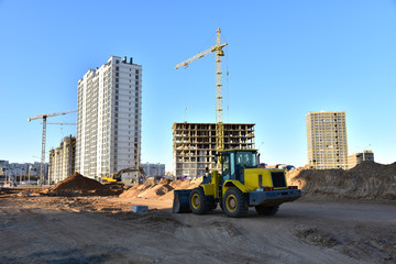 Front-end loader and excavator on road work. Tower crane in action at construction site. Earth-moving heavy equipment for road work. Construction machinery for public works, civil engineering