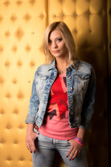 Blonde girl in jeans suit on a background of gold color. Female studio portrait.