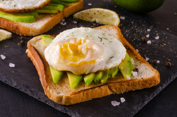 Avocado sandwich with scrambled eggs on dark background