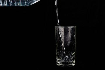 Close up pouring purified fresh drink water from the bottle isolated on black background
