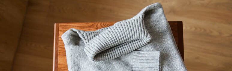 top view of grey knitted soft sweater on wooden table in room, panoramic shot
