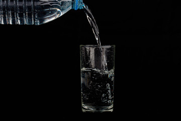 Close up pouring purified fresh drink water from the bottle isolated on black background