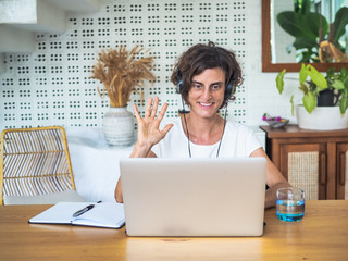 happy smiling remote woman talking, flirting and waving with headset, laptop, notebook, pen and...