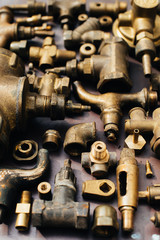 Brass scrap metal: taps, tees, plugs and various plumbing parts, spare parts. Against the background of a copper sheet. Close-up.