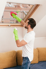 Side view of man using detergent and rag while cleaning window in living room