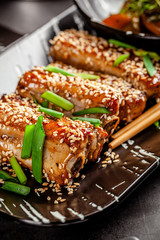 Asian food. Fried pork ribs in sweet and sour sauce with sesame seeds. Beautiful dish in a restaurant in a flat black plate. Background image. copy space