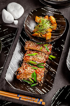 Asian food. Fried pork ribs in sweet and sour sauce with sesame seeds. Beautiful dish in a restaurant in a flat black plate. Background image. copy space