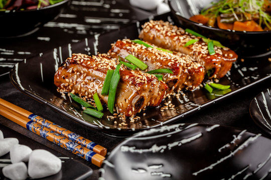 Asian food. Fried pork ribs in sweet and sour sauce with sesame seeds. Beautiful dish in a restaurant in a flat black plate. Background image. copy space