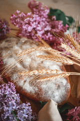 Homemade bread on a wooden table next to it, a rolling pin,spikelets of wheat and a branch of lilac. Gentle toning.