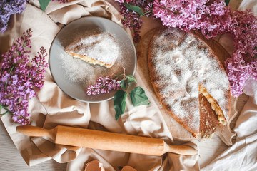 Homemade Apple pie on a wooden table next to a bowl of lilacs. Gentle toning.