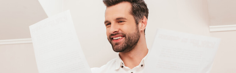 Fototapeta premium Panoramic crop of smiling teleworker looking at documents at home