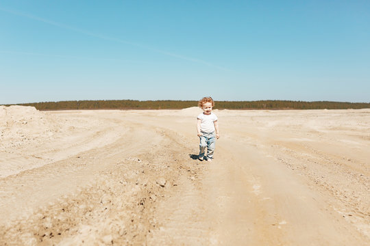 A little girl at the age of 2 walks along the sandy desert in jeans and a white T-shirt. Clear sunny day.