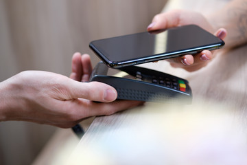 Close up of female client hold smartphone paying for order using modern easy nfc technology, waiter give card reader machine for customer make payment transaction with cashless contactless method.