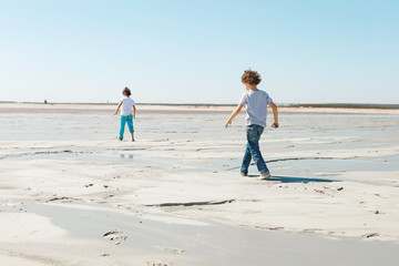 Fototapeta na wymiar 2 boys in jeans run along the coast from the list of Sunny Summer Day
