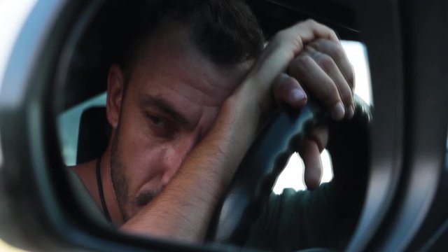 The man put his head on the steering wheel. Reflection in the mirror. A close-up. Sadly looks forward and thinks. Bad mood. Daylight is cold. 1920 x 1080.