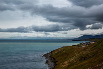 Sea landscape in Iceland. The water is clear blue and low clouds dot the deep blue sky. We can see...